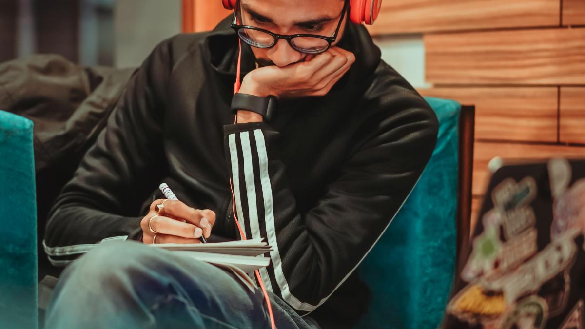 young man with headphone writing in a notebook