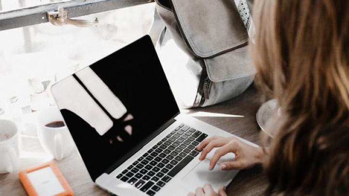 person looking at laptop with bags and phone next to her